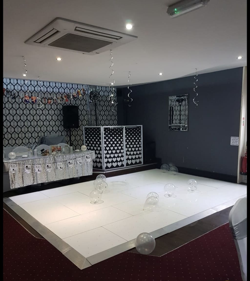 A white dance floor laid across the function room carpet in front of the stage, with the top table and a DJ booth behind