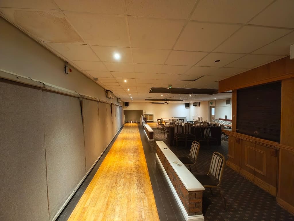 The skittle alley lit down its length, the polished lane running away from the camera with tables and seating along the right