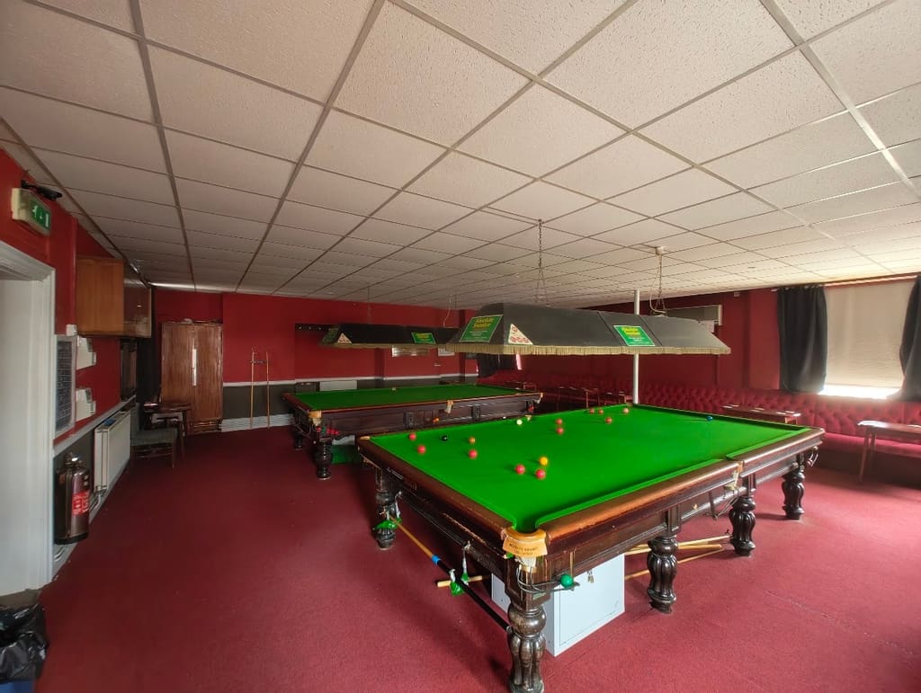 The snooker room, two full-size tables under shaded lights against deep red walls